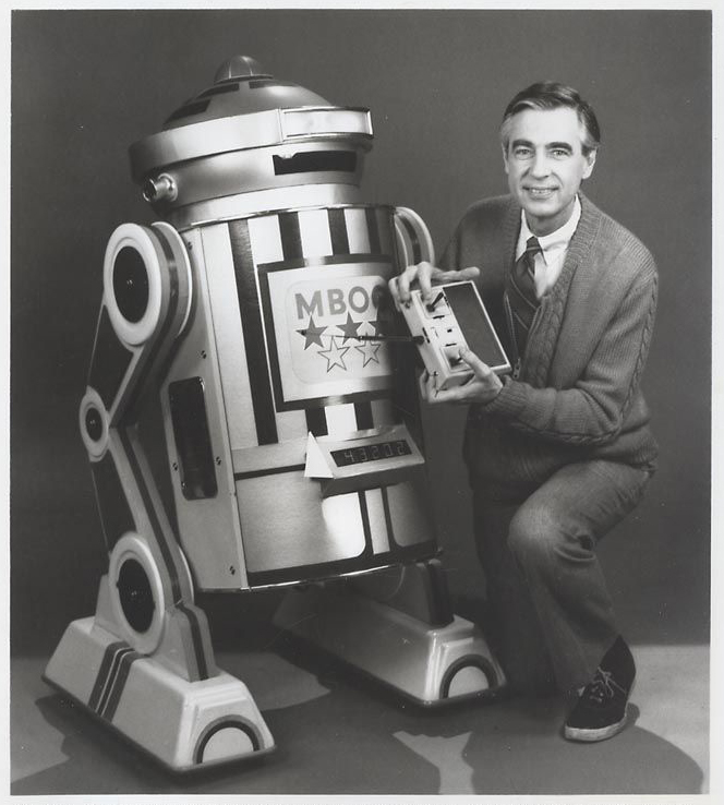 Fred Rogers kneeling to the right of a robot